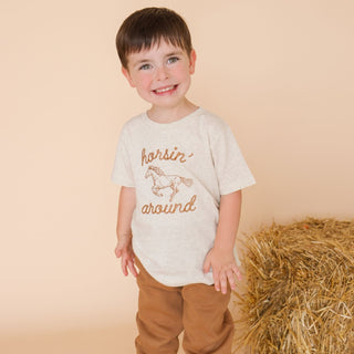 Sweet Wink Horsin' Around Western Short Sleeve T-Shirt
Child wearing a shirt with 'horser around' text standing next to a hay bale on a beige background