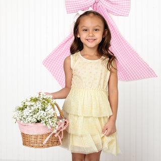 Sweet Wink Lemon Floral Tank Tutu Dress
Young girl in a yellow dress holding a basket of flowers with a large pink bow in the background.