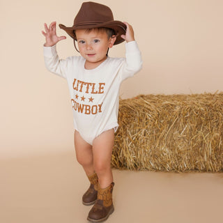 Sweet Wink Little Cowboy Western Long Sleeve Romper
Child wearing a 'Little Cowboy' outfit with a cowboy hat and boots, standing in front of hay bales.
