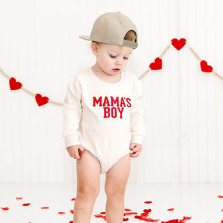 Sweet Wink Mama's Boy Varsity Patch Valentine's Day Long Sleeve Romper - Natural
Child wearing a 'Mama's Boy' onesie with heart decorations in the background.