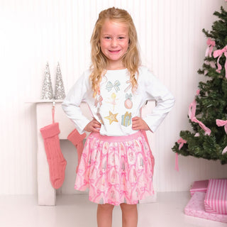 Sweet Wink Nutcracker Cutie Christmas Long Sleeve Shirt - White
Young girl in a white shirt with colorful designs and a pink skirt standing in front of a Christmas tree and stockings.