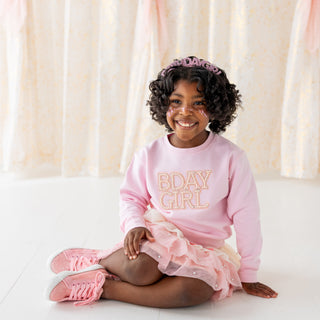Sweet Wink Pearl BDay Girl Patch Sweatshirt - Ballet
Young girl wearing a pink 'BDAY GIRL' sweatshirt and pink shoes with a tiara, sitting on a white surface with a soft, blurred background.