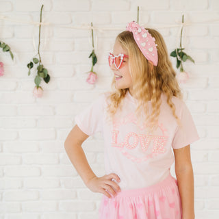 Sweet Wink Pearl Love Patch Valentine's Day Short Sleeve T-Shirt - Ballet
Young girl wearing a 'LOVE' shirt and pink skirt with heart sunglasses and headband against a white brick wall.