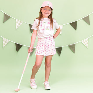 Sweet Wink pink bow athletic skort with front bow detail, shown on a model paired with a matching pink baseball hat and casual athletic top.