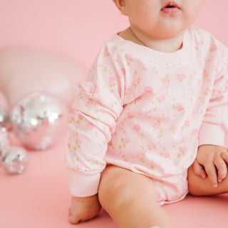Sweet Wink Pink Rose Long Sleeve Romper - Pink
Baby in a pink floral outfit sitting on a pink surface with silver balloons in the background.