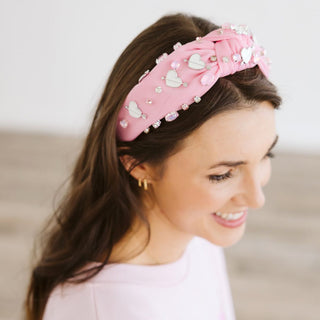 Sweet Wink Pink Valentine's Day Gemstone Headband - Large
Woman wearing a pink headband with heart decorations on a blurred background