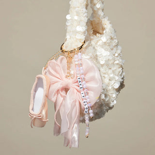 Little Words Project Bag Charm - Take It Slow
A close-up of a white sequined handbag with a dangling keychain featuring a pale pink satin bow, a miniature pink ballet flat, and a beaded charm that reads 'FAKE IT FOLLOW'.