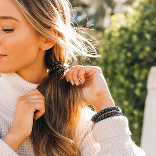 Teleties Jet Black Hair Ties - Large
Woman adjusting her hair with a blurred green background
