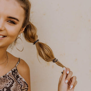 Teleties Jet Black Hair Ties - Tiny
Woman with a ponytail holding a hair tie against a beige background