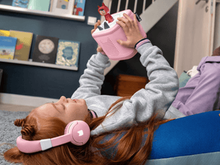 Tonies Bluetooth Headphones: Cloud Pink
Child wearing pink headphones lying on a couch with a toy in hand
