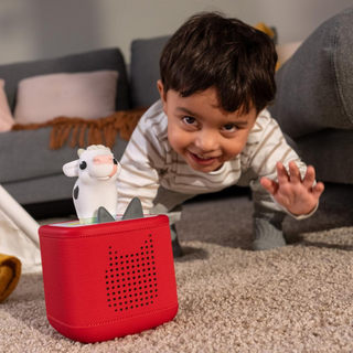 Child playing with a red toy box and a cow figurine on a carpeted floor.