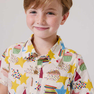 Pink Chicken Girls Jennifer Dress - Birthday Star Child wearing a colorful shirt with star and cupcake patterns on a plain background