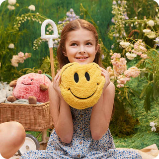 Smiley Face Warmies
Young girl holding a yellow smiley face pillow in a garden setting
