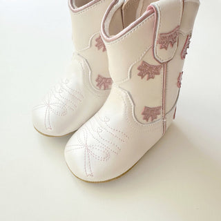 Wild & Rae cowgirl baby booties in white with pink bows, featuring soft leather and adorable western-style design for infants.