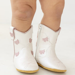 White baby cowgirl boots by Wild & Rae with pink bows, featuring soft leather and adorable Western-style design.