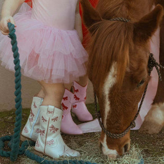 White cowgirl boots by Wild & Rae with pink bows, featuring a stylish Western design and decorative stitching.