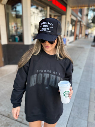 Support Your Local Mother® Trucker Hat - Black
Woman wearing a black sweatshirt and cap, holding a Starbucks cup on a sidewalk.