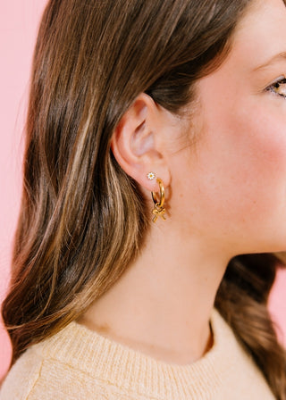 Pierced Co. White Tiny Daisy Earrings
Close-up of a person wearing gold hoop earrings with a blurred pink background