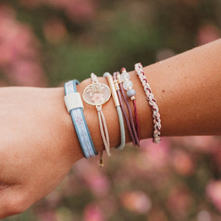 K'lani "Bloom" Maroon & Pink with Pressed Flowers Hair Tie Bracelets
Close-up of a wrist wearing multiple colorful bracelets with a blurred floral background