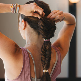 K'lani "Breathe" Lotus Flower Earthy Tones Hair Tie Bracelets
Person braiding their hair with a blurred background