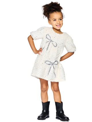 Baby Sara Tiered Dress with Sequin Bow Detail
Young girl wearing a white dress with a bow and black boots on a light gray background