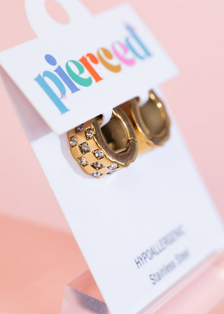 Pierced Co Huggies earrings with chunky checkered diamond pattern, featuring gold-tone metal and small sparkling stones.