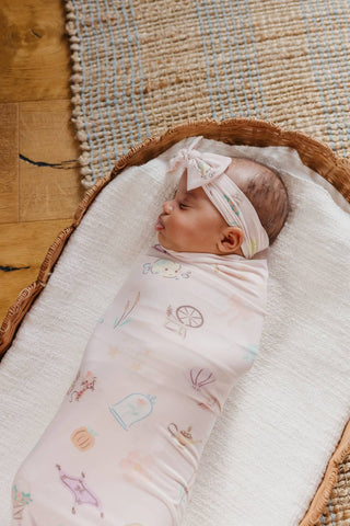 Copper Pearl Disney Enchanted Friends Knit Swaddle Blanket
Newborn baby swaddled in a pink blanket with cartoon designs, wearing a matching headband, in a wooden crib.