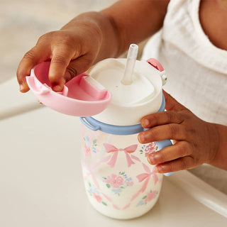 Itzy Ritzy Itzy Sips™ Straw Cup - Ribbons & Boses
Child's hand holding a floral-patterned sippy cup with a pink lid and straw.