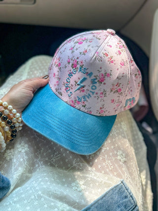 Strong As A Mother® Canvas Hat - Floral
Pink floral cap with blue brim held by a hand inside a vehicle.