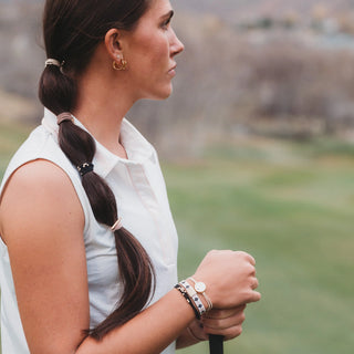 K'lani "Drive" Black & Cream Hair Tie Bracelets with Removable Ball Marker
Woman with braided hair holding a golf club on a golf course