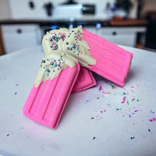 The Lavish Goat Popsicle Prize Bath Bomb - Pink
Pink ice cream cone with white scoop on a white surface with colorful sprinkles.