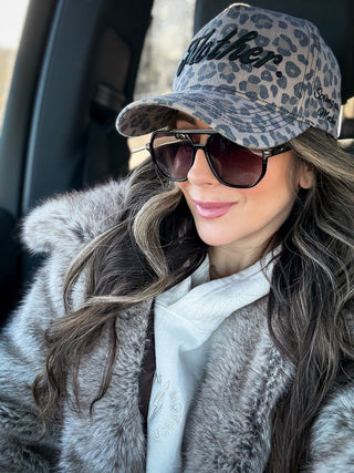 Strong As A Mother® Canvas Hat - Leopard
Woman wearing a leopard print cap and sunglasses, sitting inside a vehicle.