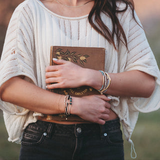 K'lani "Flirt" Polka Dot in Cream and Black Hair Tie Bracelets
Woman holding a leather-bound book in a natural setting