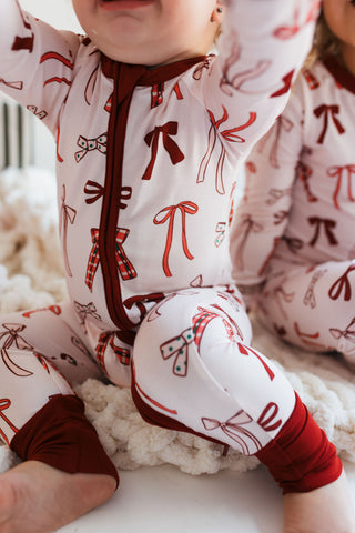 In My Jammers Merry Little Bows Zipper Romper
Children wearing pajamas with red bows on a white surface