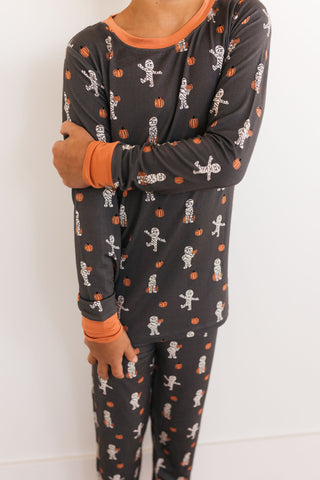 In My Jammers Mummy Two Piece Set Person wearing black pajamas with skeleton and candy corn pattern on a white background