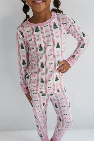 In My Jammers Pinkmas Two Piece Set 
Child wearing a festive pajama set with Christmas tree and bow pattern on a plain background