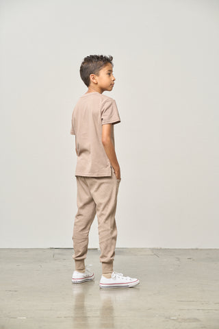 Little Bipsy Elevated Tee - Mushroom
Child wearing a beige outfit standing against a white wall.