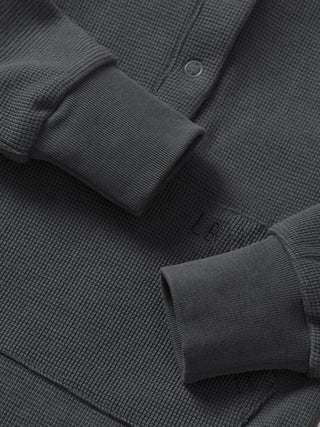 Little Bipsy Waffle Romper - Shadow
Close-up of a dark gray textured shirt with rolled-up sleeves on a matching fabric background.