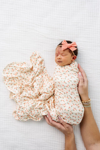 Lou Lou and Company Swaddle Blanket - Lottie
Newborn baby swaddled in a floral blanket with a pink bow on a white textured background