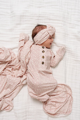 Lou Lou and Company Knotted Gown - Flora
Baby in a pink floral outfit and headband lying on a white textured surface