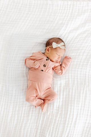 Lou Lou and Company Top and Bottoms - Abby
Newborn baby in a pink outfit with a bow lying on a white textured surface
