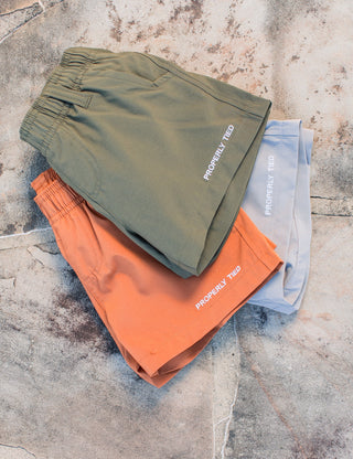 Properly Tied Boys Pintail Short - Sandstone
Three pairs of shorts in green, orange, and blue on a textured stone surface.