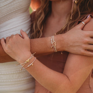 K'lani "Mother / Daughter" Pink with Pearls and Gold Hearts Shareable Hair Tie Bracelets
Close-up of two people holding hands with visible bracelets on a blurred background