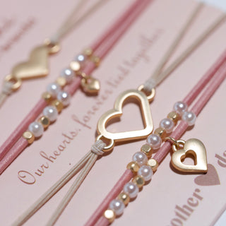 K'lani "Mother / Daughter" Pink with Pearls and Gold Hearts Shareable Hair Tie Bracelets
Bracelets with heart-shaped charms on pink strings against a matching background