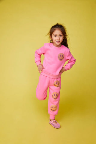 Mini Dreamers Naomi Crystal Smiley Face Sweatshirt and Sweatpant Set
Young girl wearing a pink outfit with smiley face designs on a yellow background