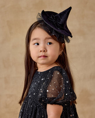 Noralee Luna Dress - Night Sky
Young girl wearing a black witch hat and dress with star patterns on a beige background