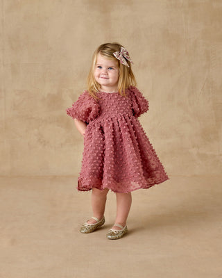 Noralee Luna Dress - Raspberry
Young girl in a pink dress with a floral headband against a beige background