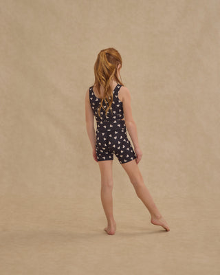 Play by Rylee & Cru Swift Sports Bra - Hearts
Young girl wearing a navy blue romper with white patterns on a beige background