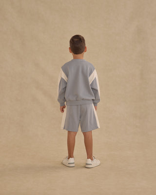 Play by Rylee & Cru Relaxed Sweatshirt - Dusty Blue
Child wearing a light blue tracksuit with white stripes on a beige background