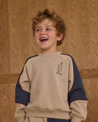 Play by Rylee & Cru Paneled Sweatshirt - Stone Child wearing a beige and navy sweatshirt with a logo against a wooden background